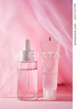 A transparent bottle of cosmetic gel and a bottle of serum on a pink background. A transparent bottle of cosmetic gel and a bottle of serum on a pink background. 105715744