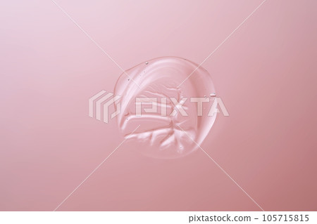 Drop of cosmetic transparent gel on a pink background. The texture of the serum, heir gel or hyaluronic booster. Drop of cosmetic transparent gel on a pink background. The texture of the serum, heir gel or hyaluronic booster. 105715815