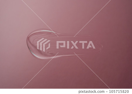 Drop of cosmetic transparent gel on a pink background. The texture of the serum, heir gel or hyaluronic booster. Drop of cosmetic transparent gel on a pink background. The texture of the serum, heir gel or hyaluronic booster. 105715820