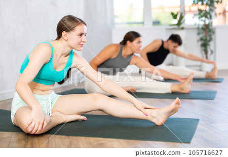 Slim young girl practicing head to knee pose of yoga on black mat 105716627