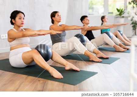Women and man maintaining physical health practicing pilates with fit balls at group workout Women and man maintaining physical health practicing pilates with fit balls at group workout 105716644