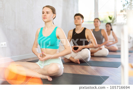 Slim young girl practicing lotus pose of yoga on black mat Slim young girl practicing lotus pose of yoga on black mat 105716694