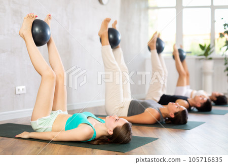 Young girl practicing pilates pose with softball between legs in training area 105716835