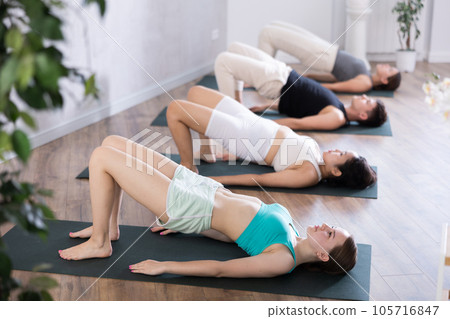 Young teen woman in company of hatha yoga lovers performs bridge pose, setu bandha sarvangasana 105716847