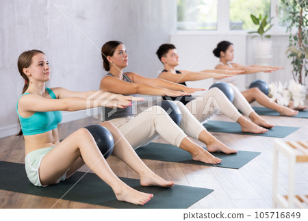Girl is doing Pilates in the studio. People lie on their backs holding a soft ball pilates in their outstretched legs Girl is doing Pilates in the studio. People lie on their backs holding a soft ball pilates in their outstretched legs 105716849
