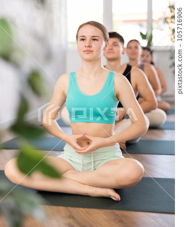 Young lady performs comfortable half-lotus pose, Ardha padmasana Young lady performs comfortable half-lotus pose, Ardha padmasana 105716906