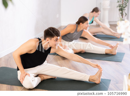 Yoga class of sports women and man performing Head to Knee Forward Bend Pose, or Janu Sirsasana after practicing together Yoga class of sports women and man performing Head to Knee Forward Bend Pose, or Janu Sirsasana after practicing together 105716990