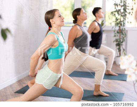 Slim young girl practicing warrior pose of yoga on black mat 105716992