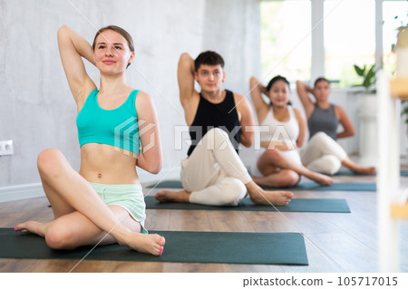Slim young girl training cow face pose of yoga on black mat Slim young girl training cow face pose of yoga on black mat 105717015