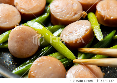 A cooking scene where frankfurter sausage and garlic sprouts are fried. 105720532