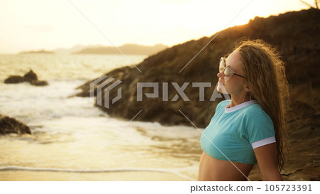Woman leaning on a rock reef enjoying the warm golden sunset. Wo 105723391