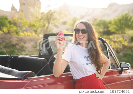 beautiful happy girl in a skirt posing near a retro car in the mountains of cappadocia with a metal can of coca cola 105724691
