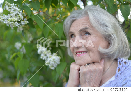 Portrait of a senior woman in a hat and blouse on the background of a blooming lilac bush Portrait of a senior woman in a hat and blouse on the background of a blooming lilac bush 105725101