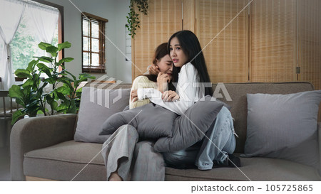 Homosexual young woman lesbian couple in sweater sitting on sofa to watching scary horror cinema while hug each other in living room at home Homosexual young woman lesbian couple in sweater sitting on sofa to watching scary horror cinema while hug each other in living room at home 105725865