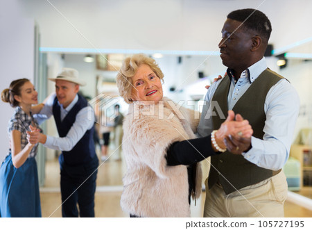 Elderly woman learning ballroom dancing in pair in dance studio Elderly woman learning ballroom dancing in pair in dance studio 105727195