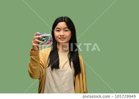 Smiling Asian teenage girl with film camera posing isolated on green background 105729949