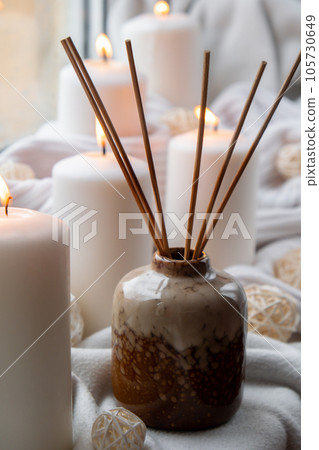 Aroma reed diffuser. Bottle container with wood stick diffusers Essential oils to scent your home fragnance concept autumn holidays at cozy home on the windowsill Hygge aesthetic atmosphere on knitted Aroma reed diffuser. Bottle container with wood stick diffusers Essential oils to scent your home fragnance concept autumn holidays at cozy home on the windowsill Hygge aesthetic atmosphere on knitted 105730649