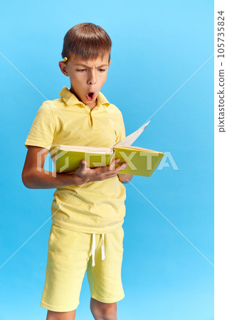 Homework time. Emotive school boy looking through book with serious and thoughtful face against blue studio background Homework time. Emotive school boy looking through book with serious and thoughtful face against blue studio background 105735824