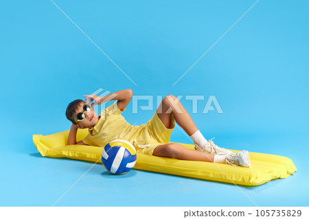 Enjoyment. Happy and relaxed little boy, child lying on swimming mattress with volleyball ball against blue studio background Enjoyment. Happy and relaxed little boy, child lying on swimming mattress with volleyball ball against blue studio background 105735829