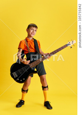 Boy, child in stylish clothes playing guitar against yellow studio background. Music and education 105735842