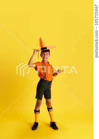 Full-length portrait of cheerful little boy, child in stylish clothes posing with smile against yellow studio background Full-length portrait of cheerful little boy, child in stylish clothes posing with smile against yellow studio background 105735847
