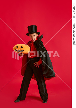 Trick or treat. Portrait of little boy, child in costume posing with pumpkin toy against red studio background 105735870