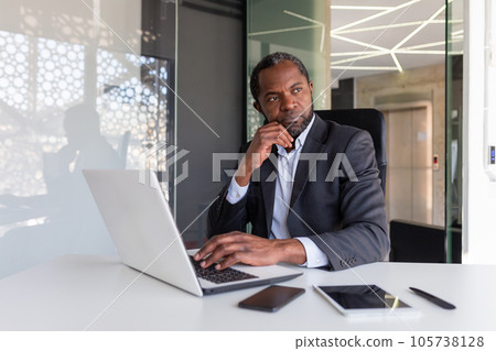 Thinking mature adult african american businessman at workplace, financier boss investor with laptop thinking about financial solutions new projects inside office. 105738128