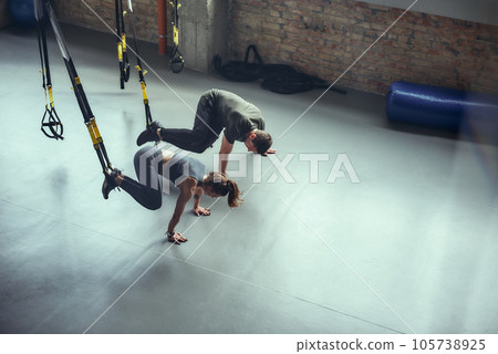 Hard workout. Man and woman in sportswear doing TRX workout at gym. Training legs with Trx fitness straps at gym 105738925
