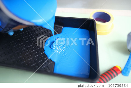 Hand pour blue paint from can into black plastic tray. 105739284