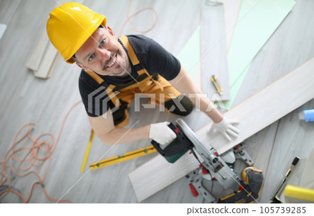 Builder in overalls and hard hat cut laminate on machine in room. Builder in overalls and hard hat cut laminate on machine in room. 105739285