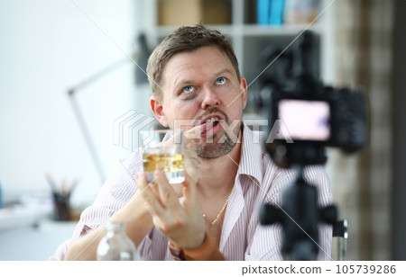 Disheveled man hold glass of alcohol in his hand and taste it with his finger. Disheveled man hold glass of alcohol in his hand and taste it with his finger. 105739286