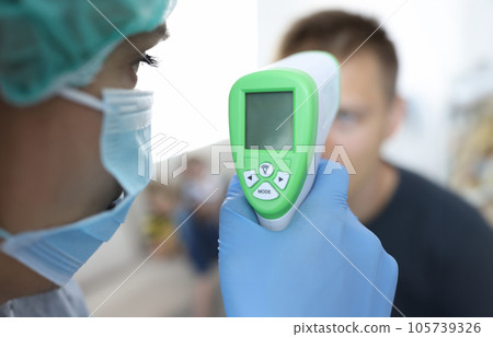 Doctor in a protective medical mask measures temperature of patient. Doctor in a protective medical mask measures temperature of patient. 105739326