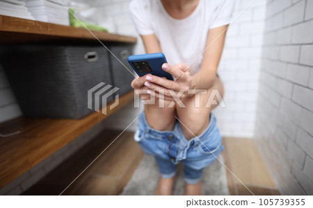 Person sits on toilet and holds smartphone in his hands 105739355