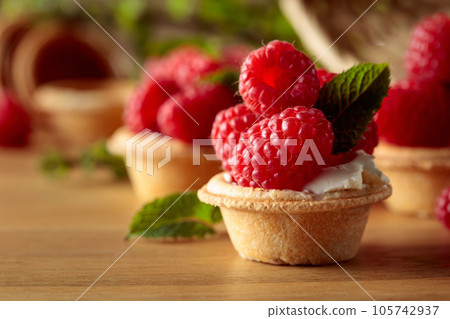 Tartlets with fresh raspberries and mint on a wooden table. Tartlets with fresh raspberries and mint on a wooden table. 105742937
