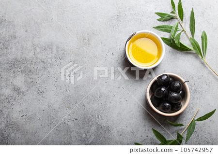 Black olives and extra virgin olive oil in little bowl with olive tree branches top view on grey concrete stone background, space for text Black olives and extra virgin olive oil in little bowl with olive tree branches top view on grey concrete stone background, space for text 105742957
