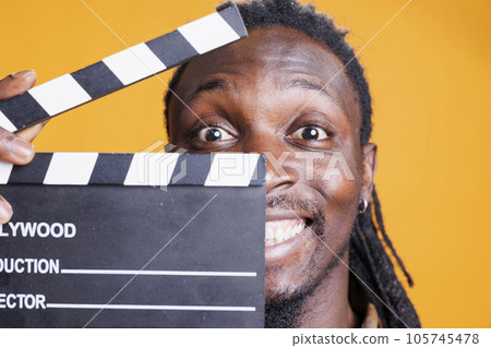 Portrait of man holding blackboard to cut scenes in movie industry, posing on yellow background. African american young adult working in film making production and cinematography 105745478