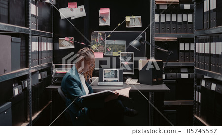 Private investigator reviewing new case evidence on detective board, conducting investigation. Woman officer examining surveillance photos and criminal records, using case files for justice. Private investigator reviewing new case evidence on detective board, conducting investigation. Woman officer examining surveillance photos and criminal records, using case files for justice. 105745537