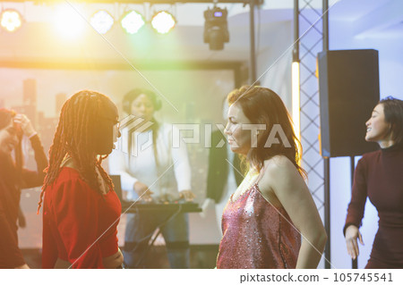 Young women doing dance battle at disco party with live electronic music in nightclub. Serious dancers standing on crowded dancefloor and improvising moves at discotheque 105745541