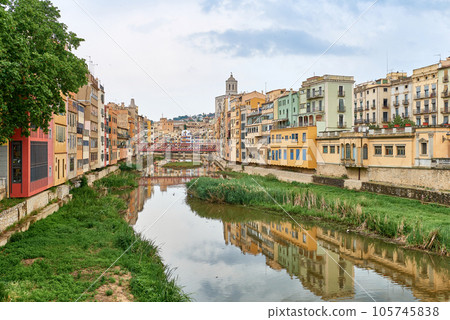 Colorful yellow and orange houses and bridge Pont de Sant Agusti reflected in water river Onyar, in Girona, Catalonia, Spain. Church of Sant Feliu and Saint Mary Cathedral at background. BRIDGE in the 105745838