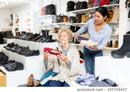 Friendly female sales consultant serves a mature woman who is going to try on shoes Friendly female sales consultant serves a mature woman who is going to try on shoes 105748447