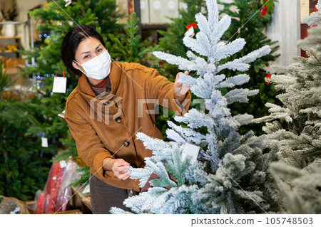 Asian woman shopper in a protective mask, chooses a Christmas tree 105748503