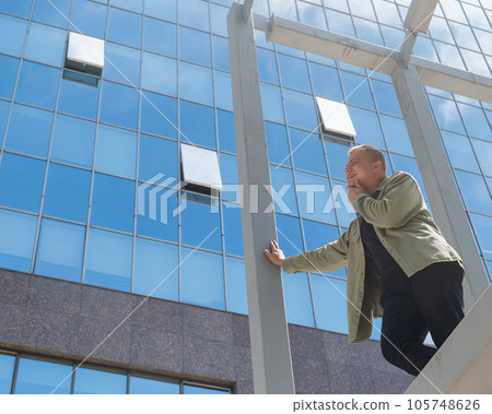A pensive man stands against the backdrop of a skyscraper. 105748626