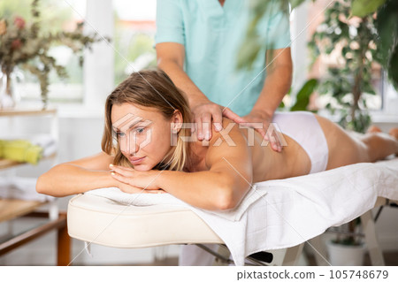 Relaxed middle-aged woman having back massage therapy conducted by skilled masseur 105748679