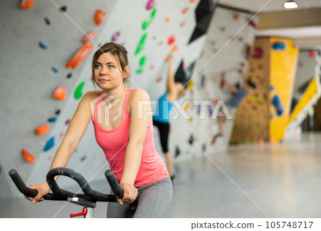 Sports girl on an exercise bike in climbing hall Sports girl on an exercise bike in climbing hall 105748717