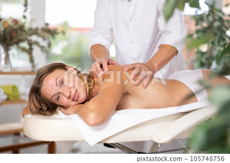 Relaxed middle-aged woman having back massage therapy conducted by skilled masseur Relaxed middle-aged woman having back massage therapy conducted by skilled masseur 105748756