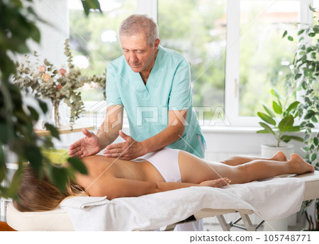 Skilled old masseur conducting back massage for woman client 105748771
