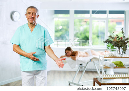 Positive old masseur posing against background of therapy room Positive old masseur posing against background of therapy room 105748997