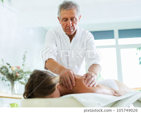 Skilled old masseur conducting back massage for woman client Skilled old masseur conducting back massage for woman client 105749026