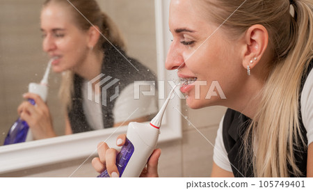 A woman with braces on her teeth uses an irrigator. Close-up portrait. A woman with braces on her teeth uses an irrigator. Close-up portrait. 105749401