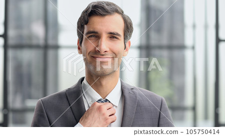 Business man adjusting his tie against the backdrop of a modern office 105750414